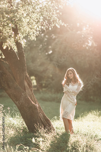 Portrait of a beautiful young blond woman in a white dress in a boho style walks in the park in summer at sunset.