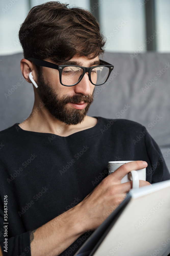 Image of focused man drinking coffee and reading magazine while sitting Image of focused man drinking coffee and reading magazine while sitting