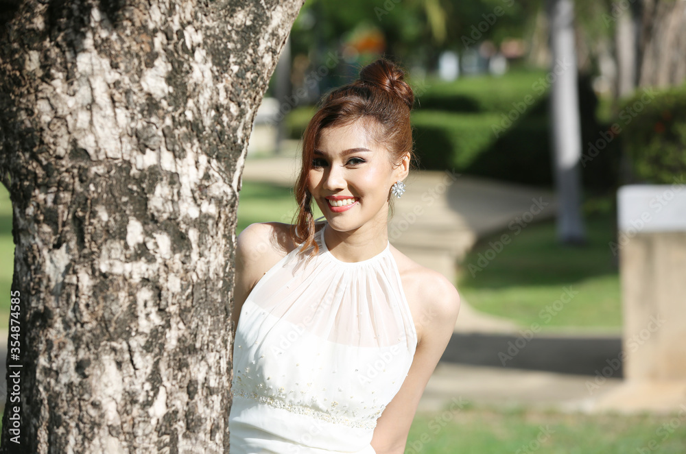 Portrait of Beautiful attractive bride in wedding dress with long full skirt standing by tree in the park Portrait of Beautiful attractive bride in wedding dress with long full skirt standing by tree in the park