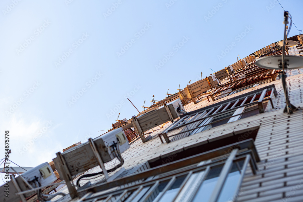 Multi-storey residential building. The front of the house is hung with air conditioning and satellite dishes. Bottom view Multi-storey residential building. The front of the house is hung with air conditioning and satellite dishes. Bottom view