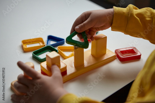 The boy is playing in his room. Educational game. Learning shapes and colors. A child plays with a sorter.