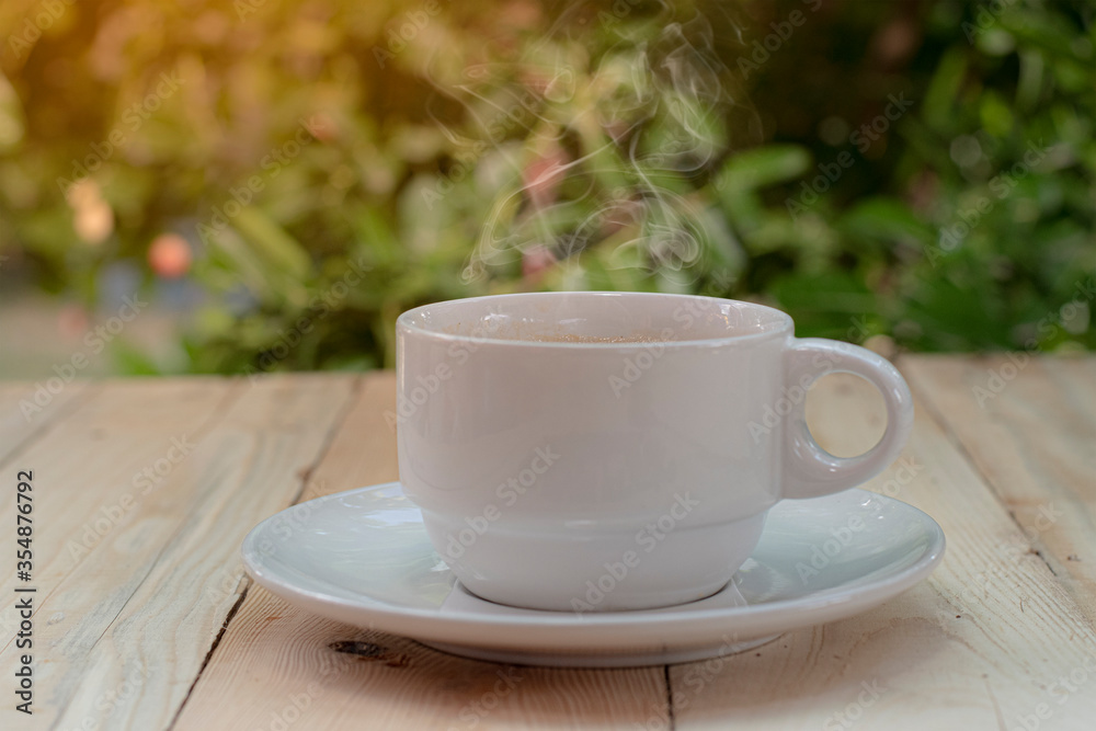 A coffee cup placed on a wooden background with a tree bokeh A coffee cup placed on a wooden background with a tree bokeh