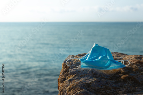Covid-19 face mask on a rock with out of focus sea background