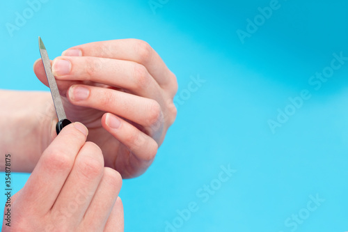 Hands of a caucasian woman polishing her nails with a nail file on a blue background, close-up, copy space.