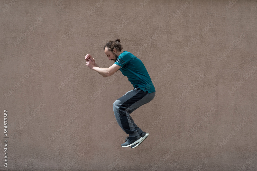 young bearded guy sortsman jumping on the background of a pink street wall