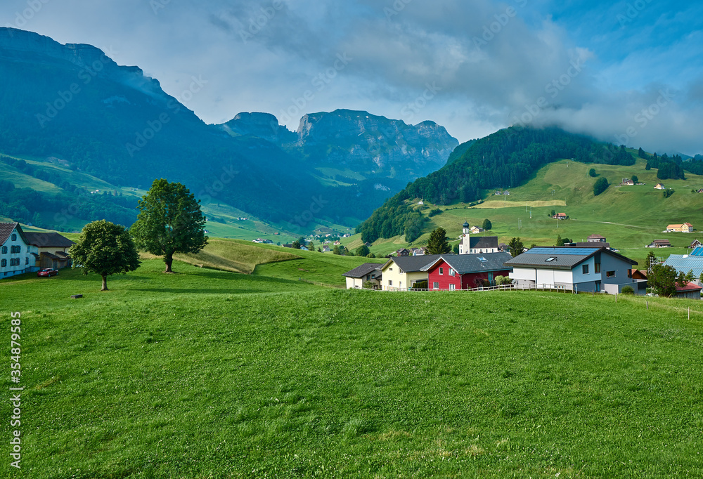 Landscape panorama of green nature and village houses near Appenzell, Alpstein mountains, Switzerland. Taken in June, in summer.