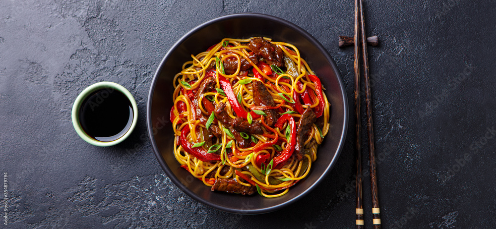 Stir fry noodles with vegetables and beef in black bowl. Slate background. Top view. Stir fry noodles with vegetables and beef in black bowl. Slate background. Top view.