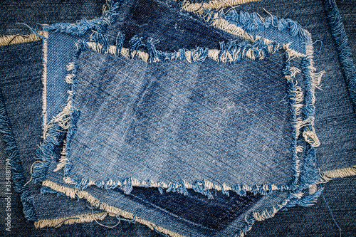 Destroyed torn denim blue jeans fabric frame on blue jeans background. Worn Jeans Casual Double Color patch Denim.