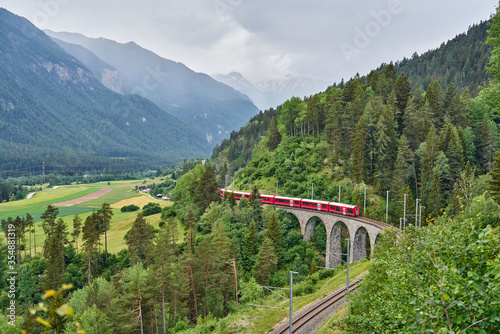 Red train passes above the Landwasser Viaduct bridge  in canton of Graub  nden  Switzerland. Bernina Express   Glacier Express uses this railroad.
