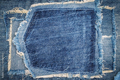 Destroyed torn denim blue jeans fabric frame on blue jeans background. Worn Jeans Casual Double Color patch Denim.