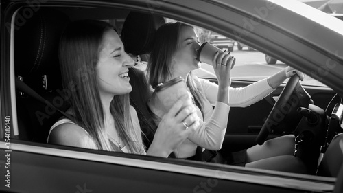 Portrait of beautiful female driver drinking coffee while driving a car with her girl friend