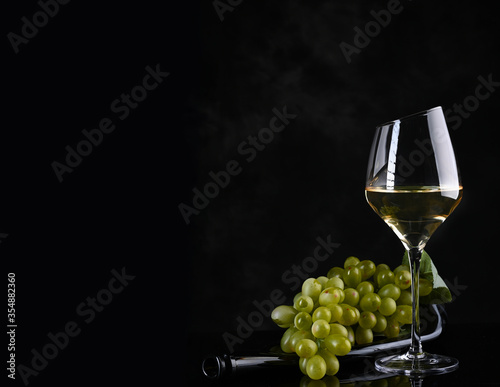 Wine background. White wine in wineglass, grape on old bottle .