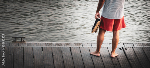 A barefoot man standing on the wooden pier contemplates the tranquility of the sea photo