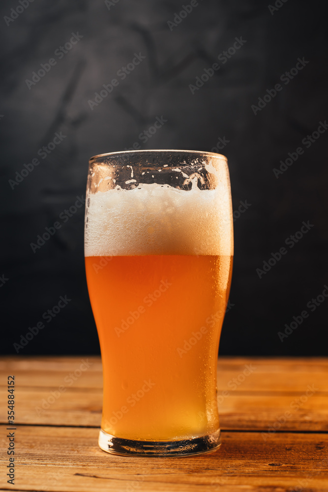 Glass of cold pale beer placed on a rustic wooden table