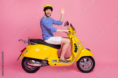 Profile side view of his he nice attractive handsome cheerful cheery glad funky guy driving moped having hi hello greetings having fun isolated over pink pastel color background © deagreez