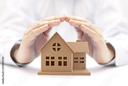 Property insurance. House miniature covered by hands.