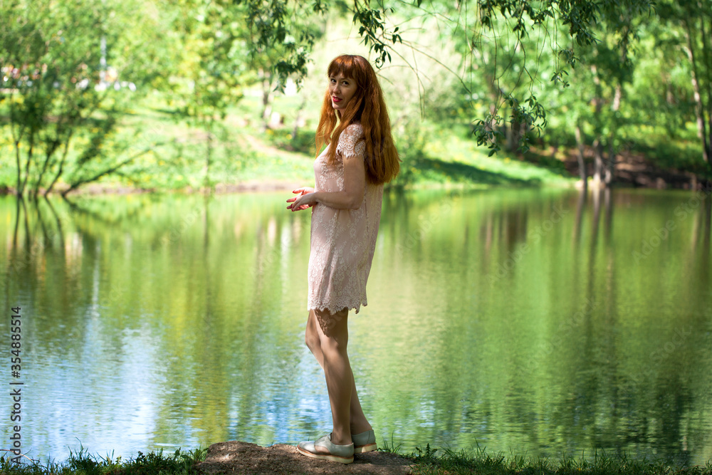 Fototapeta premium Portrait of a young beautiful woman in white dress posing by the lake