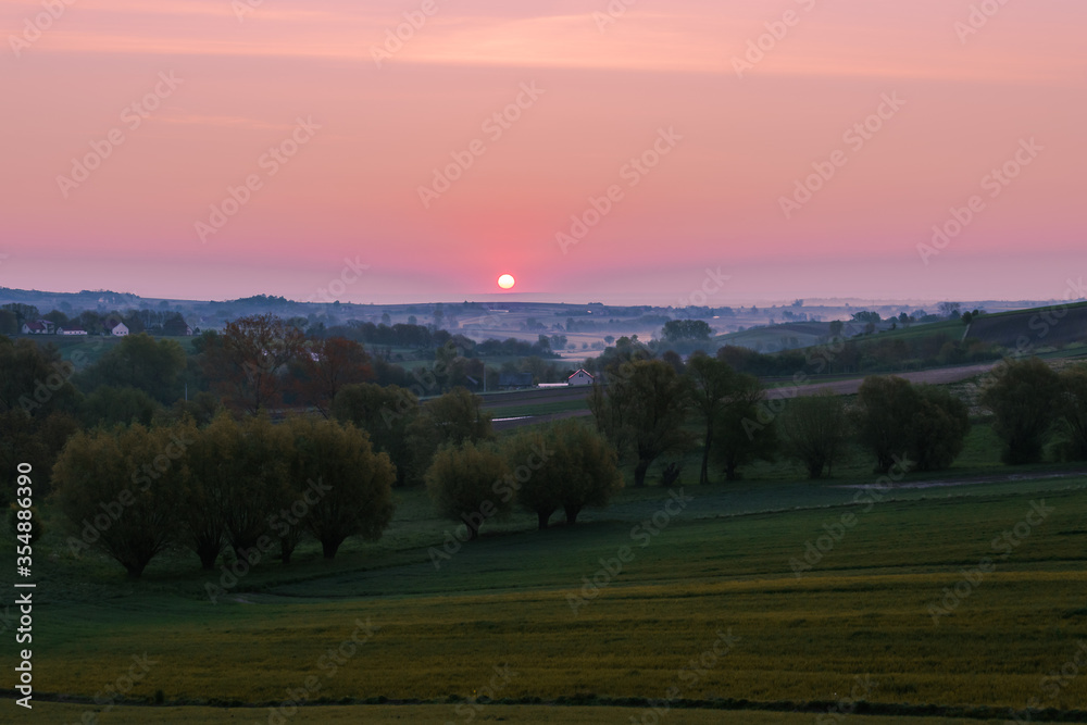 Colorful countryside landscape with the rising sun over the fields and trees.