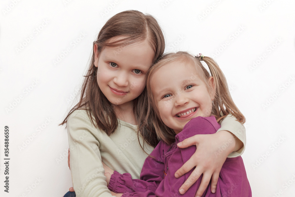 Two little girls sisters smiling and hugging on a light background Two little girls sisters smiling and hugging on a light background