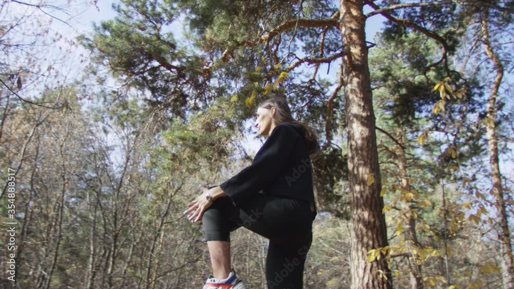 4K portrait of good-looking female in sportswear doing high knees exercises in sunlit forest at autumn morning. Low angle 360 degree tracking arc shot. 4K portrait of good-looking female in sportswear doing high knees exercises in sunlit forest at autumn morning. Low angle 360 degree tracking arc shot.