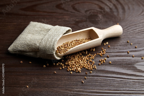 Buckwheat groats (hulled seeds) in burlap bag, scoop on wooden background