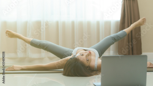 Billede på lærred Woman doing a workout, lying on the floor doing power stretching exercises for her legs with video clip on laptop