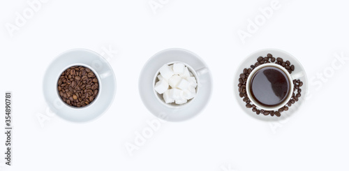 Set of white cups with saucers with coffee beans, coffee and sugar cubes isolated on a white background, top view.