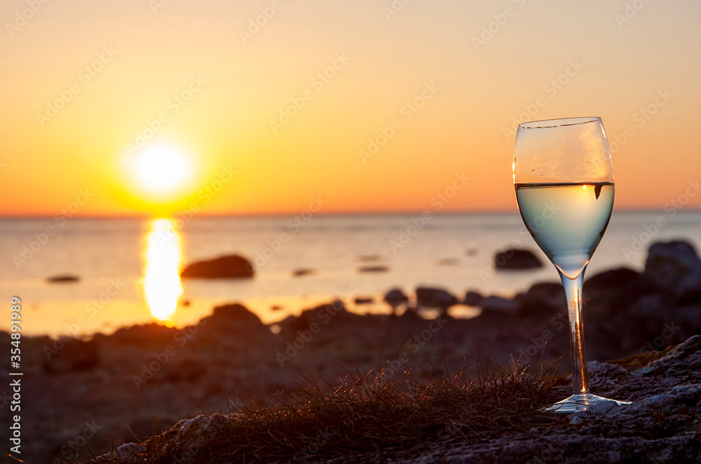 Wine glass standing on a cobblestone beach with ocean sunset background