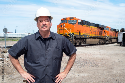 Male worker wearing hard hat standing in front of diesel train locomotive in train yard  photo