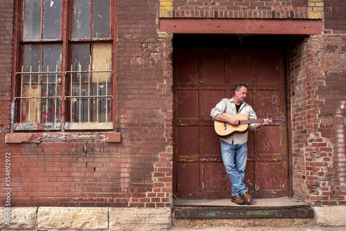 Man playing acoustic guitar standing on factory loading dock in city