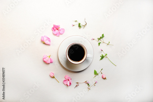 White mocha cup with coffee on white cloth. Centered with copy space on left and right side. Pink flower petals form a circle around the beverage. High angle view.