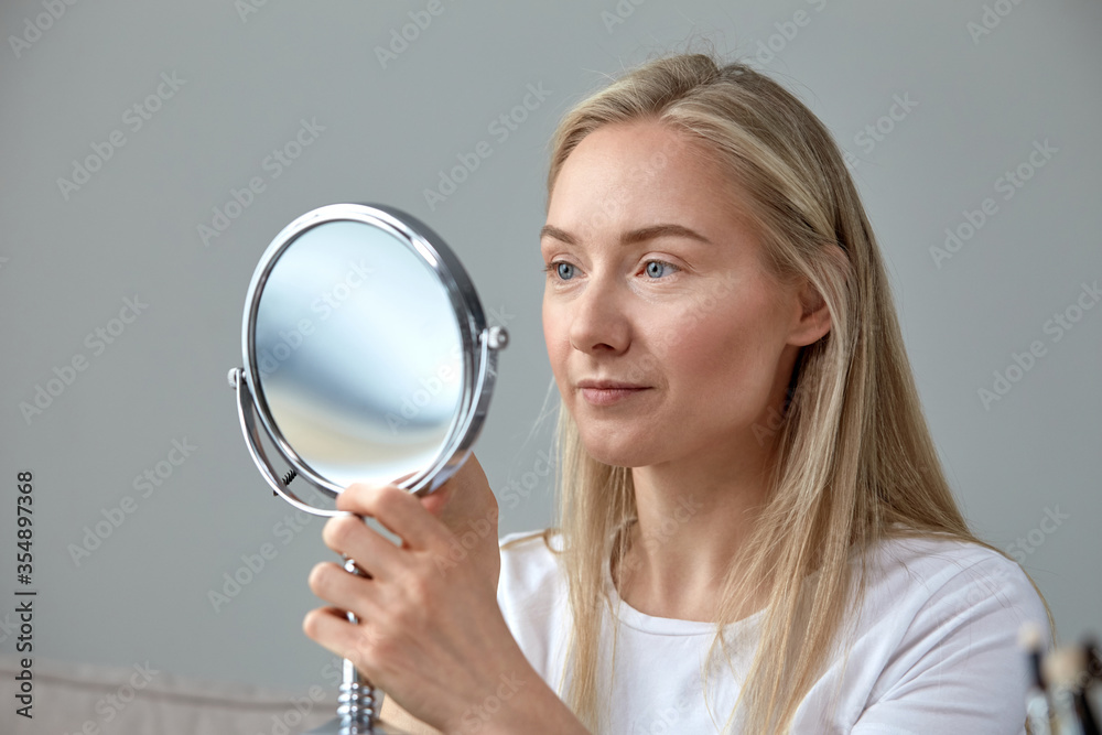 Woman natural blonde without makeup looks in a round mirror Woman natural blonde without makeup looks in a round mirror