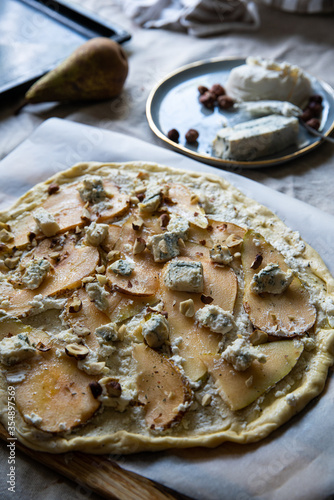 Step by step process of making pizza with pear, ricotta, gorgonzola and hazelnuts. Uncooked pizza ready to get to oven.