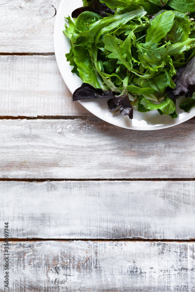 Concept of healthy food, clean eating, low calories meal, organic products. White plate with green salad on wooden background. Spinach, aragula, letucce. Top view flat lay copy space for text Concept of healthy food, clean eating, low calories meal, organic products. White plate with green salad on wooden background. Spinach, aragula, letucce. Top view flat lay copy space for text