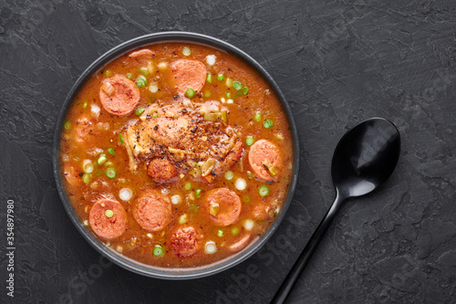 Chicken and Sausage Gumbo soup in black bowl on dark slate backdrop. Gumbo is louisiana cajun cuisine soup with roux. American USA Food. Traditional ethnic meal photo