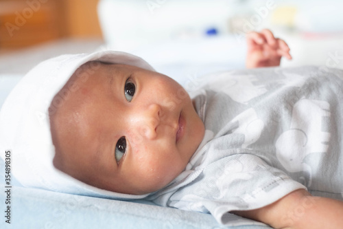 Portrait Photo of happy newborn baby infant with big black eyes lay down on the bed