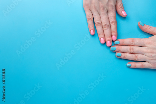 Women s hands with bright summer manicure on a blue background. Trendy colors of nail polishes for young women. Copy space