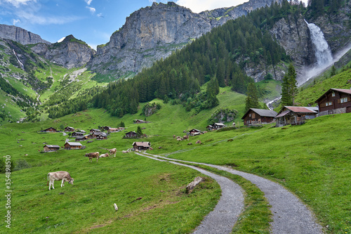 Fotografie Beautiful landscape panorama from Swiss Alps, with cows, waterfall, meadow and farm houses