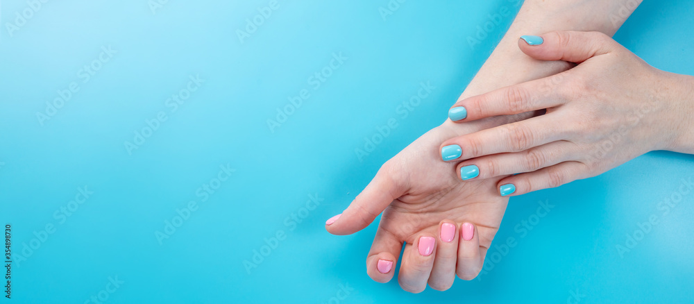 Women's hands with bright summer manicure on a blue background. Trendy colors of nail polishes for young women. Copy space Women's hands with bright summer manicure on a blue background. Trendy colors of nail polishes for young women. Copy space
