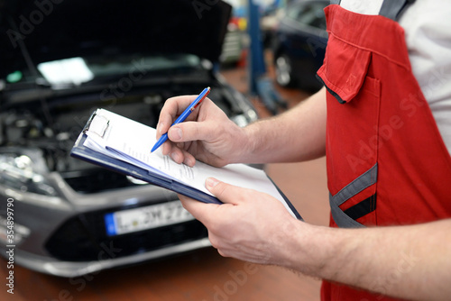 Foto KFZ Mechaniker überprüft ein Fahrzeug in der Werkstatt - checkliste Funktion //