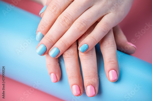 Women s hands with bright summer manicure on a blue and pink background. Trendy glamorous nails in fun colors