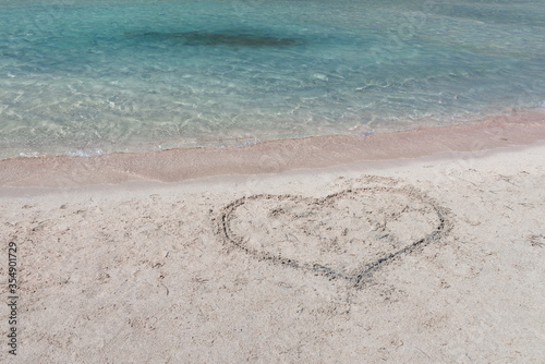 Heart drawn on the pure white and pink sand beach with magical turquoise waters, in lagoon on Crete, Greece. Romantic holiday concept