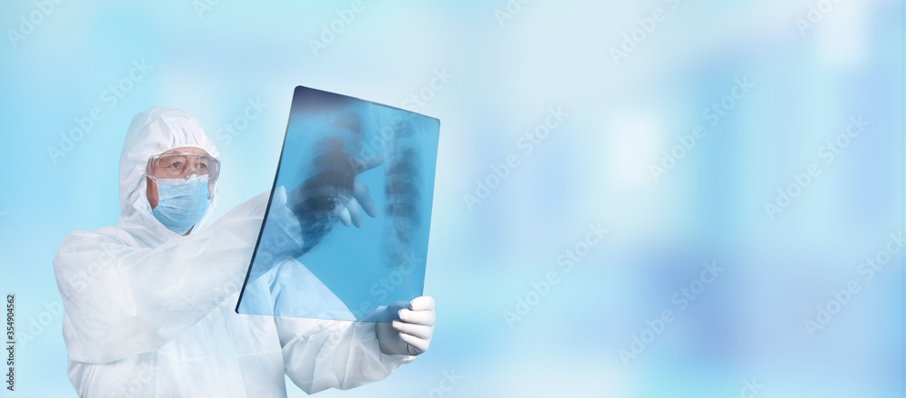 Doctor in PPE suit uniform examines an X-ray of a patient s lung infected with covid-19 coronavirus, pneumonia. Healthcare and medicine concept.