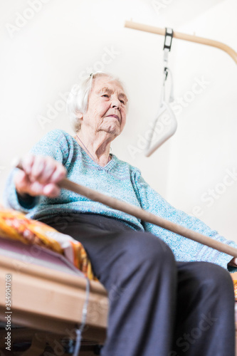 Elderly 96 years old woman exercising with a stick sitting on her bad. Geriatric health care home assisted support for older people concept. Care for the elderly.