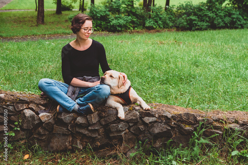 Fotografie The girl is sitting in an embrace with a Labrador Retriever and smiles