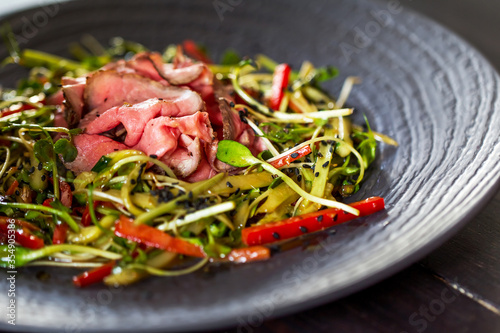 Authentic salad with bacon fresh red pepper, sprouts, sesame and olive oil on a black plate. Morning atmospheric lighting, fashionable trendy spot soft focus. Preparation for design creative menu.