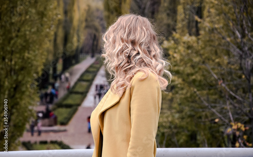 Blonde young girl stands on the bridge and looks at the park with an alley. © Тетяна Клімчук