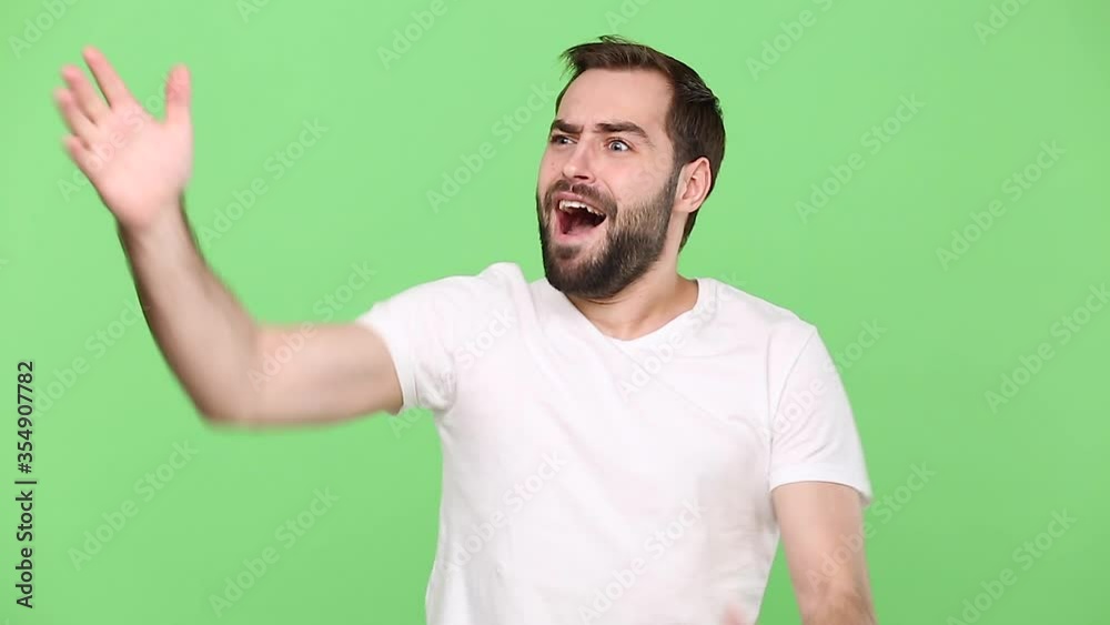 Shocked bearded young guy 20s in white t-shirt isolated on green chroma key background studio. People sincere emotions lifestyle concept. Looking at clock watch gets nervous realizes that he is late Shocked bearded young guy 20s in white t-shirt isolated on green chroma key background studio. People sincere emotions lifestyle concept. Looking at clock watch gets nervous realizes that he is late