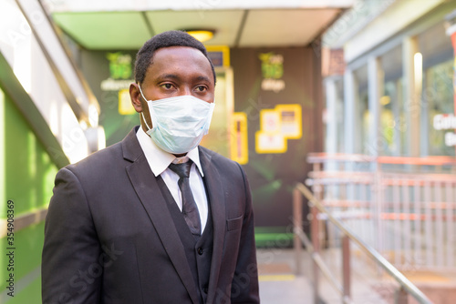 Portrait of African businessman with mask thinking at the train station outdoors
