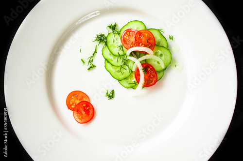 Cherry tomato, cucumber and onion salad on a white round plate. Vegetables are cut into slices
